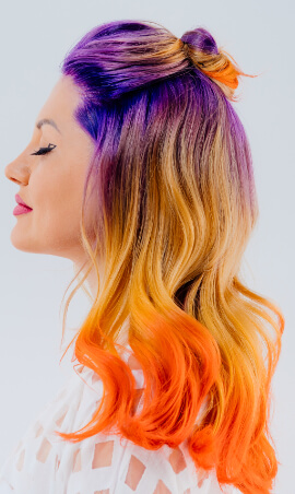 Oldalról fotózott hölgy arca lila, sárga és narancssárga árnyalatú hajjal